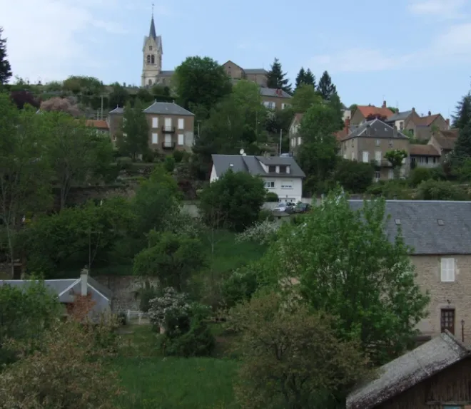 Village perché sur une colline arborée, dominé par une église au clocher visible au sommet.