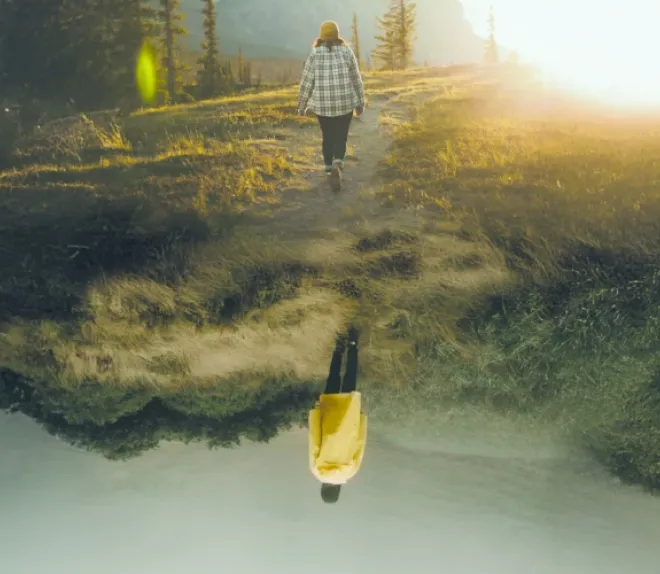 Personne marchant sur un sentier en montagne au soleil, avec une silhouette inversée en reflet créant un effet surréaliste.