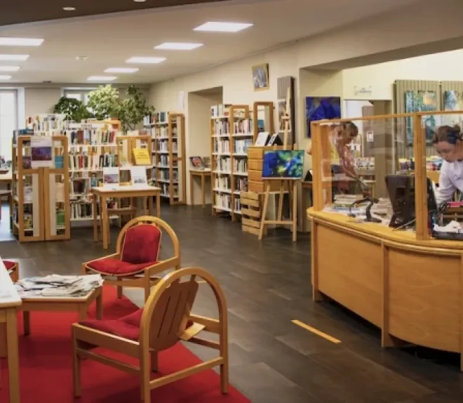 Vue intérieure d’une bibliothèque avec des rayonnages de livres, un espace de lecture et un comptoir d’accueil.